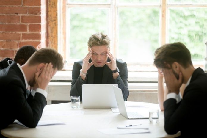 Angespannte Geschäftsrunde mit drei Personen und Laptops am Konferenztisch